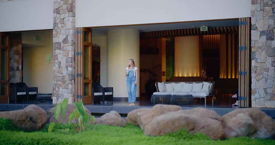 Stylish young woman sips a green smoothie in the open-air lobby of a luxurious resort, enjoying a tranquil moment
