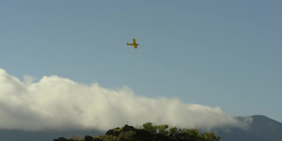 A plane flies above clouds and hills