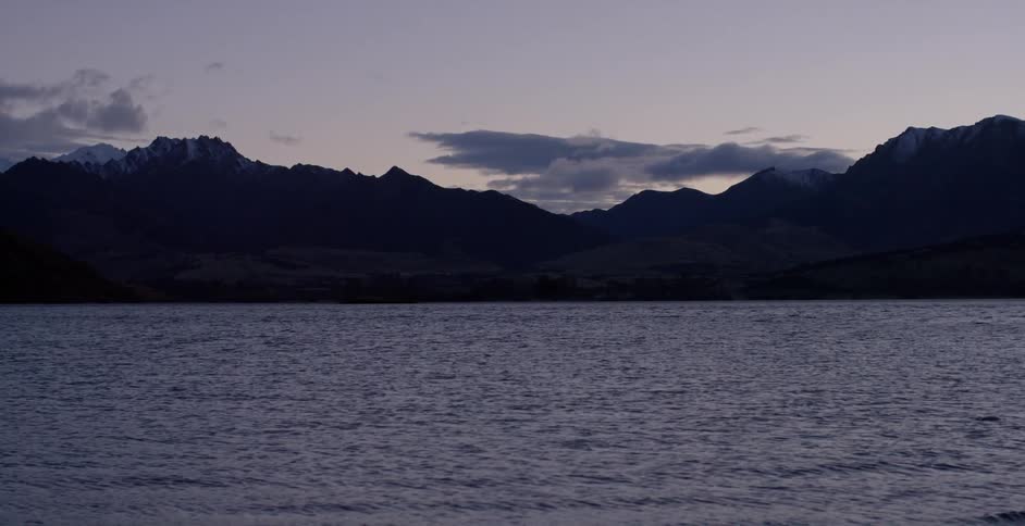 Water flows and waves roll in the ocean near some mountains at dusk