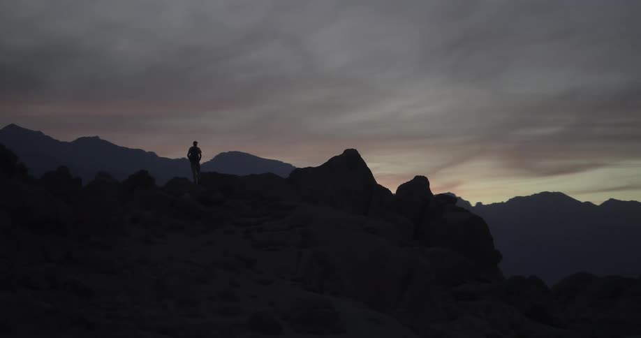 A slow pan reveals a silhouetted hiker walking along a rocky mountain ridge at dawn