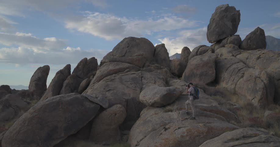 A man with a backpack photographs the dramatic scenery from a rocky outcrop in a vast mountain landscape