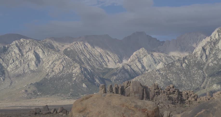 A lone hiker with a backpack stands among giant boulders, gazing at the majestic Sierra Nevada mountain range