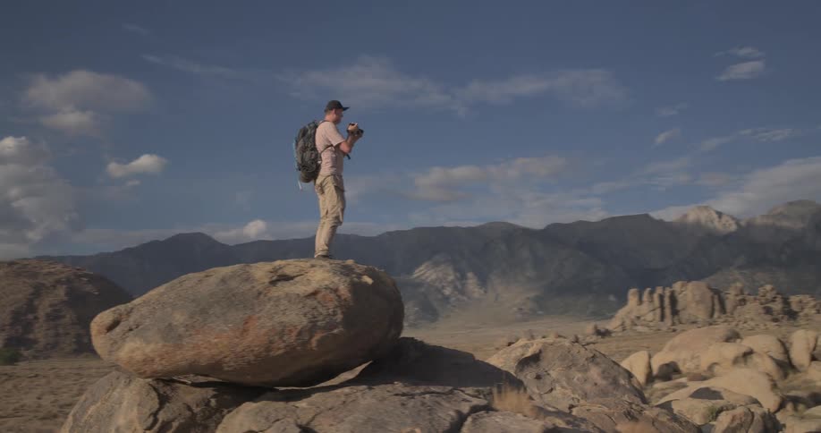 Adventurous hiker and photographer captures the vast mountain landscape from a balanced rock in the desert