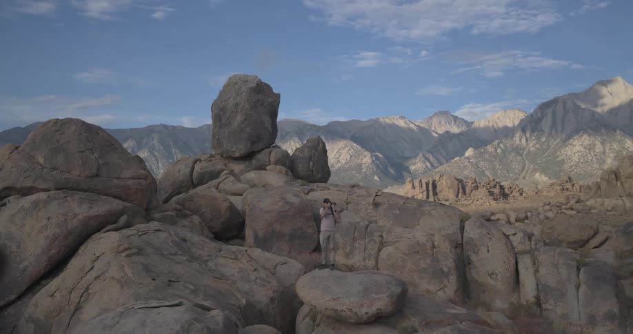 A lone photographer explores a vast rocky landscape, capturing the beauty of the distant mountain range under a blue sky