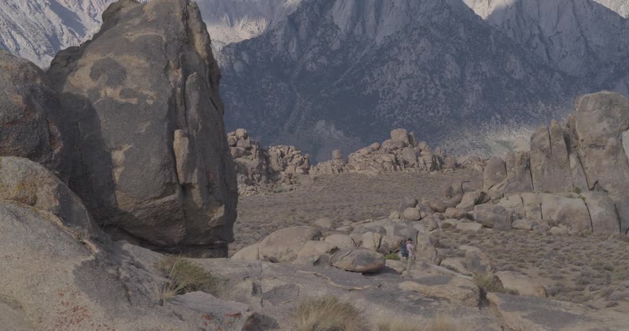 A lone hiker with a backpack traverses the rugged, rocky terrain of Alabama Hills with the Sierra Nevada mountains in the background