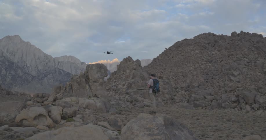 A lone adventurer with a backpack pilots a drone through the stunning, rocky landscape of the Alabama Hills at twilight