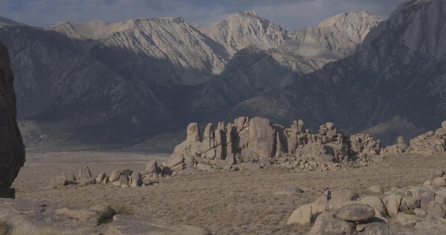 A lone hiker stands on a boulder in the Alabama Hills, admiring the majestic Sierra Nevada mountains in the distance as the camera slowly zooms in