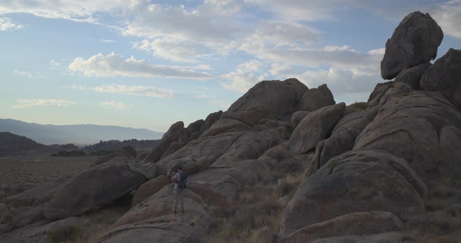A lone hiker stands atop a giant boulder in the Alabama Hills, photographing the vast and rocky desert landscape