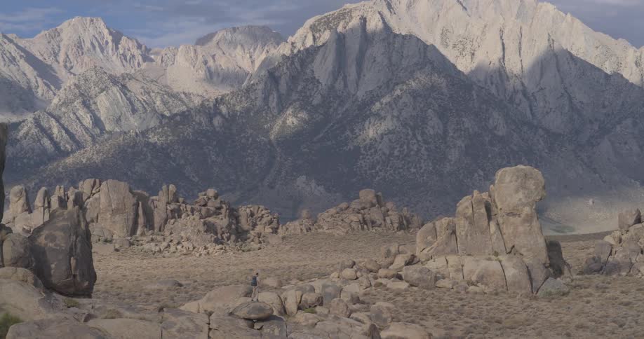 A lone hiker explores the unique rocky landscape of the Alabama Hills, dwarfed by the immense Sierra Nevada mountain range in the background