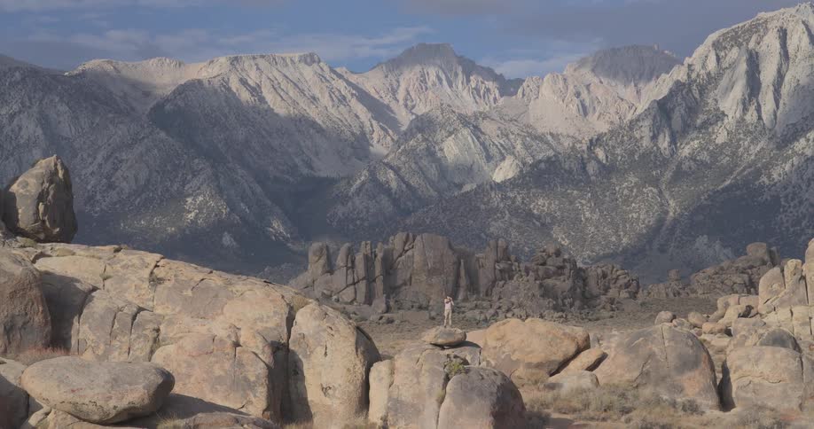 A lone photographer stands on a rocky outcrop, capturing the magnificent view of the towering Sierra Nevada mountains