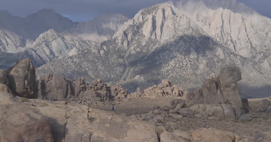 A lone hiker with a backpack stands on a rock formation, gazing at the majestic Sierra Nevada mountains in the distance