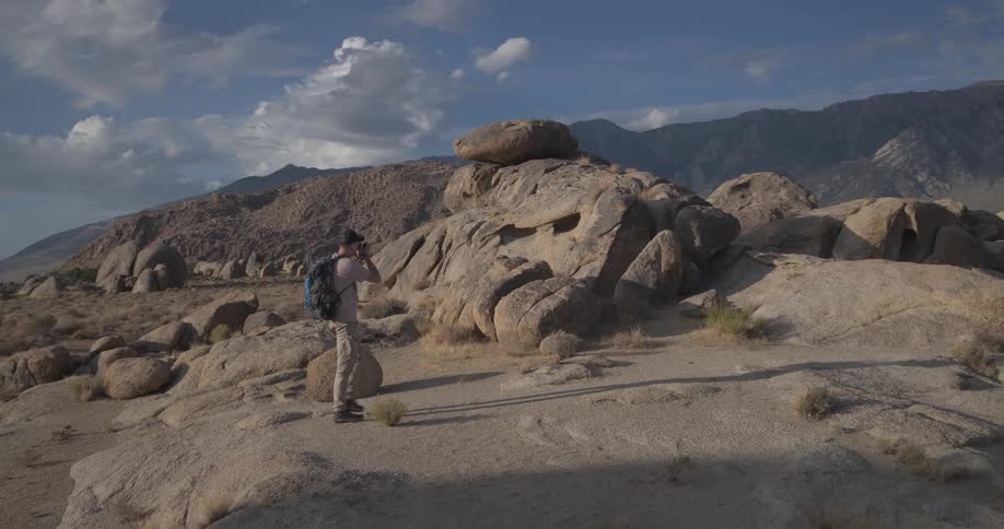 A hiker and photographer explores the unique rock formations of the Alabama Hills with mountains in the background