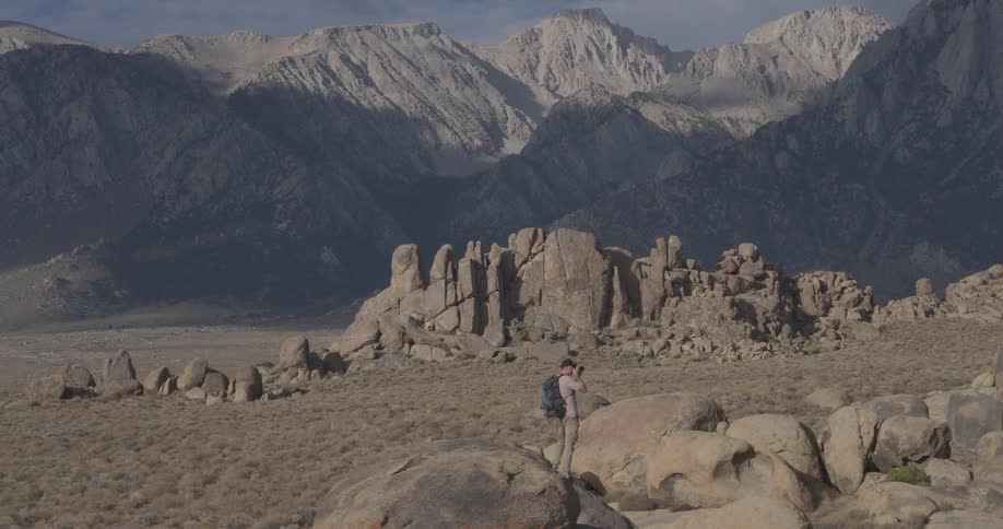 A photographer with a backpack takes photos of the rocky landscape as the camera pulls back to reveal the majestic Sierra Nevada mountains