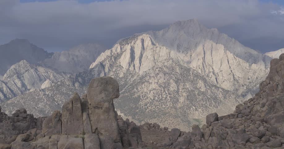 A sweeping pan across the rugged rock formations of the Alabama Hills reveals the majestic Sierra Nevada mountain range under a cloudy sky