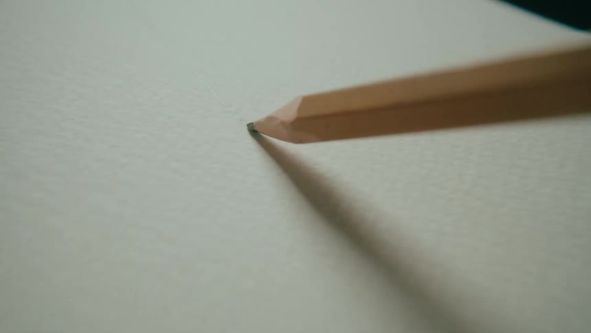 Extreme close-up of a pencil tip drawing a faint line across textured white paper