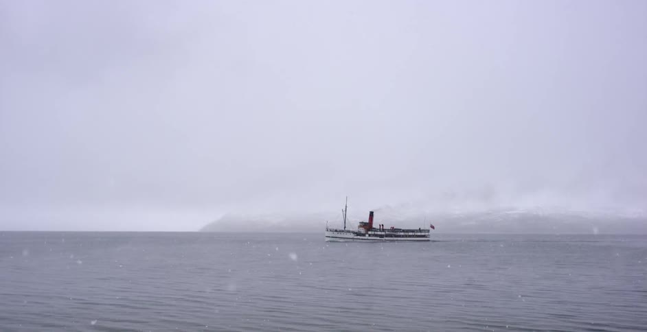 A large ship floats in the icy water as it snows