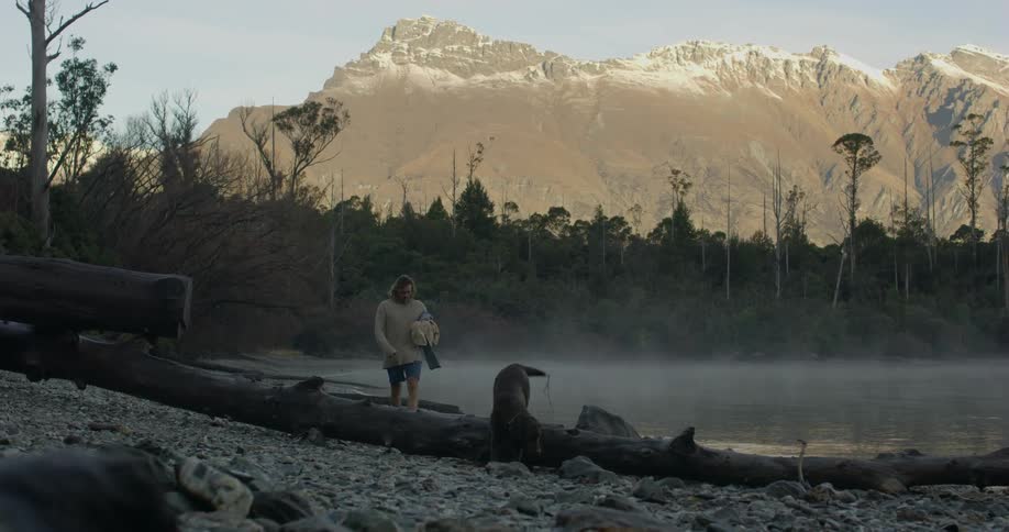 A man walks with a dog on a mountain lakeshore