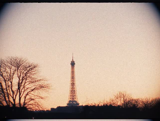 A vintage Super 8 film shot of the Eiffel Tower silhouetted against a warm sunset sky in Paris, France