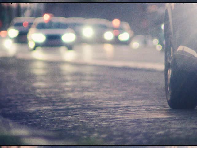 A gritty, low-angle view of out-of-focus car traffic on a wet street with glowing headlights