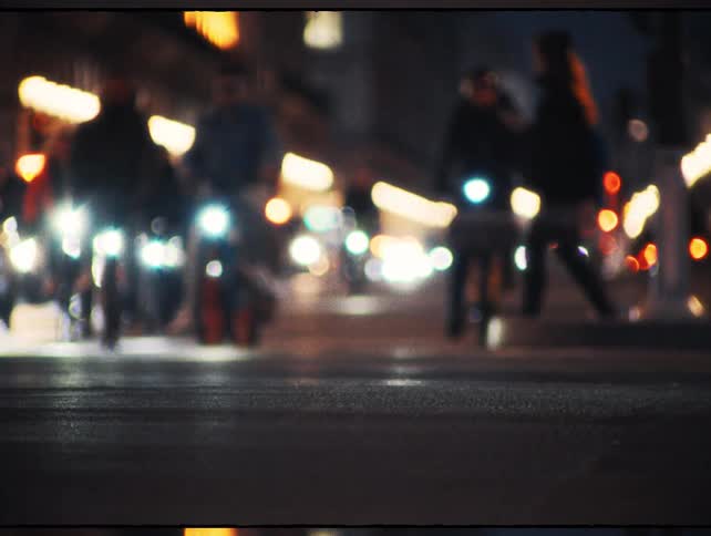 Blurred cyclists and pedestrians move through a city street at night with beautiful bokeh lights