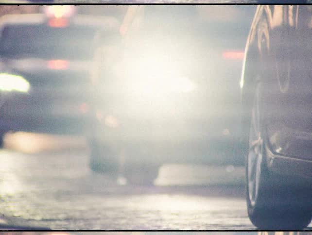 A vintage-style, blurry low-angle shot captures the movement of city traffic and a lone cyclist at dusk