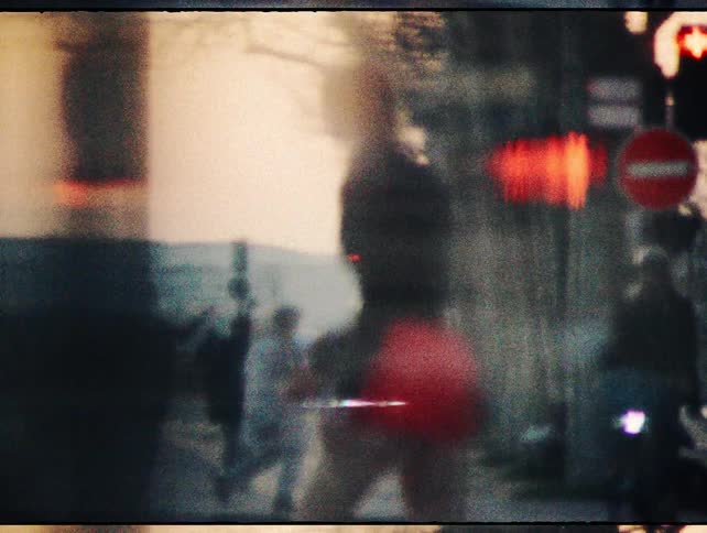 Vintage-style, grainy footage captures the abstract silhouettes of pedestrians and traffic on a city street