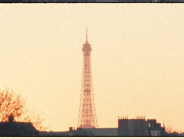 Vintage film footage zooms in from the Seine River to the iconic Eiffel Tower silhouetted against a beautiful sunset in Paris, France