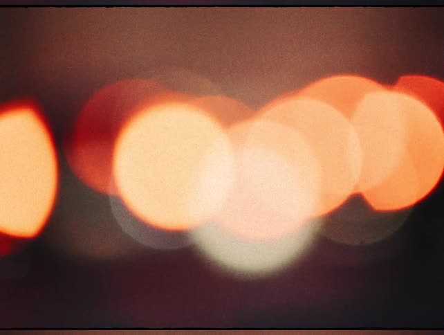 A dreamy and abstract close-up of warm orange and red bokeh lights moving with a vintage film grain