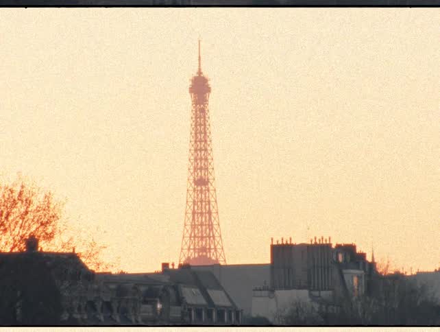 A grainy, vintage film shot of the Eiffel Tower in Paris silhouetted against a golden sunrise sky