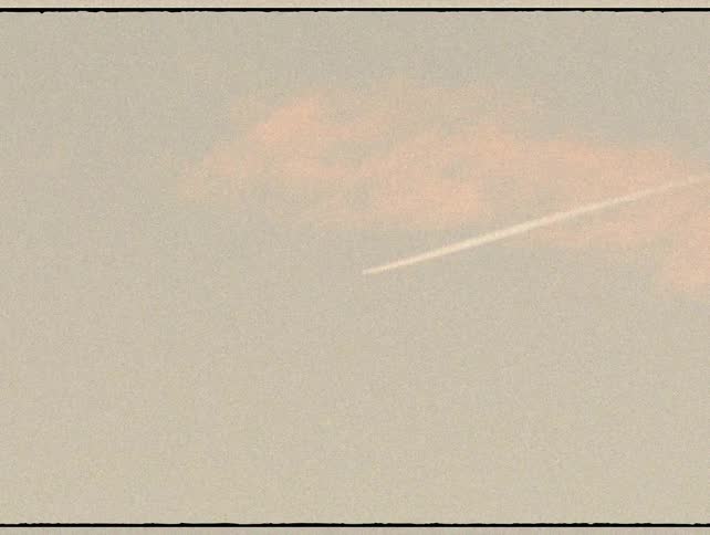 A jet leaves a contrail across a hazy, grainy sky at sunset in this vintage-style, slow-zoom shot