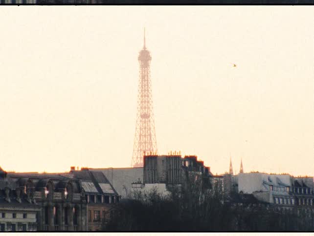 A vintage 1970s film shot of the Eiffel Tower against a hazy, warm sunset sky over the Paris skyline
