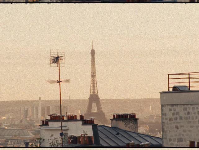 A grainy, vintage-style shot of the Eiffel Tower seen over the rooftops of Paris on a hazy day