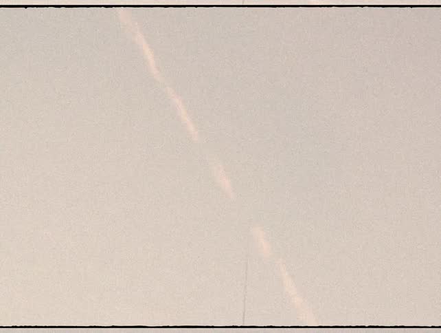 Vintage film shot pans up from the rooftops of Paris to an airplane contrail streaking across the sky