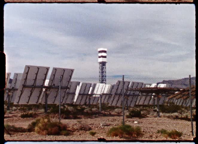 Vintage film captures a view of a solar thermal energy plant with its central tower surrounded by panels in a vast desert