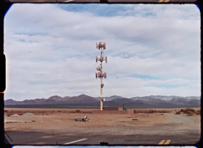 A vintage film shot of a solitary cell phone tower standing in a desolate desert landscape with mountains in the background