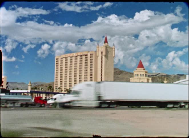 Vintage 8mm film captures a driving shot of Whiskey Pete's Hotel and Casino in the Nevada desert with trucks on the highway