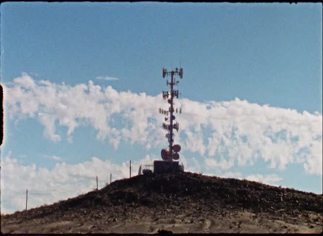 A vintage, gritty film shot captures a communication tower standing tall on a remote desert butte