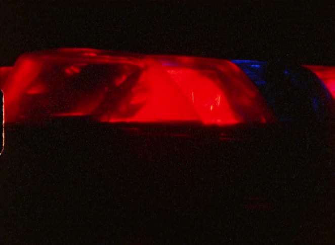 A grainy, vintage close-up of red and blue police emergency lights flashing rapidly in the dark