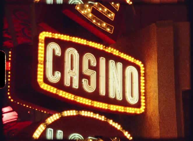 Flashing yellow and white neon lights illuminate a classic 'Casino' and 'Hotel' sign at night in this authentic vintage 8mm film footage