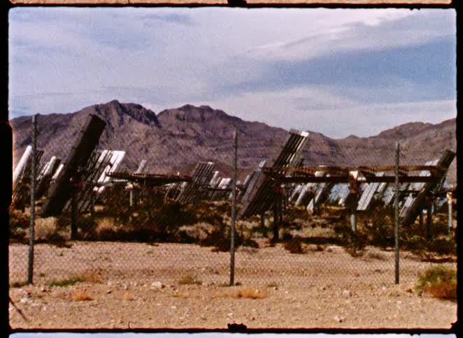 Vintage 8mm footage pans across a solar energy farm in a dry, mountainous desert landscape