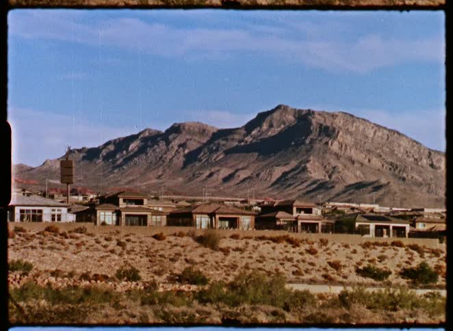 A vintage, 8mm-style shot of a suburban neighborhood in a desert landscape with large mountains in the background