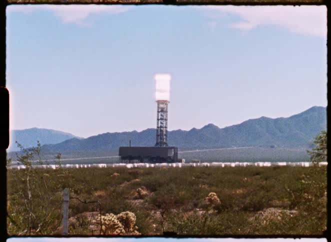 A vintage film shot captures a concentrated solar power tower glowing brightly amidst a field of heliostats in the desert