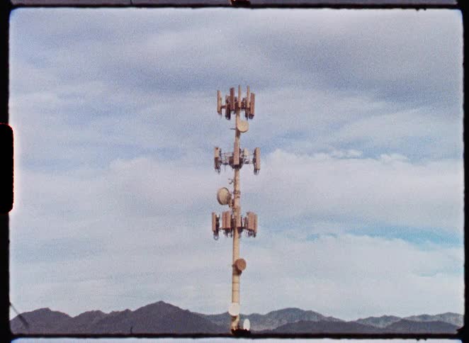 A slow zoom on a solitary cell phone tower in the middle of a vast desert landscape, captured on Super 8mm film