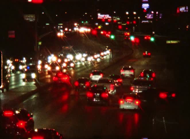 Vintage footage shows a blurry scene of heavy city traffic at night with glowing red taillights and white headlights