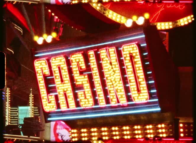 A vintage film-style shot captures the flickering red and yellow lights of a classic casino sign at night