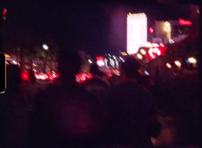 Vintage 8mm footage shows silhouetted crowds walking down the blurry, neon-lit Las Vegas Strip at night