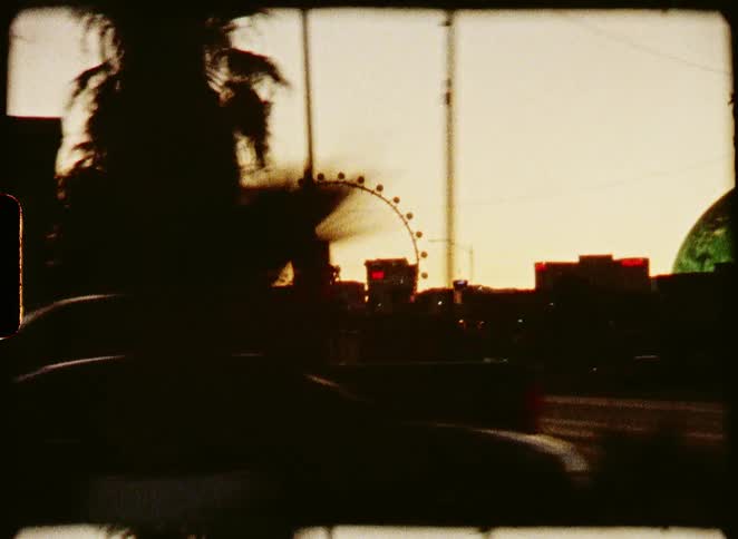 Driving through a desert city at sunset, with silhouetted palm trees and a Ferris wheel captured on grainy, vintage 8mm film