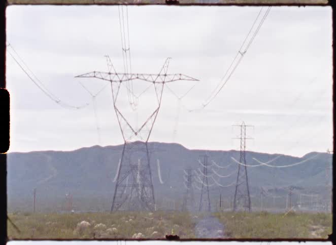 Vintage film shot of electrical transmission towers standing in a desolate desert landscape with mountains in the background