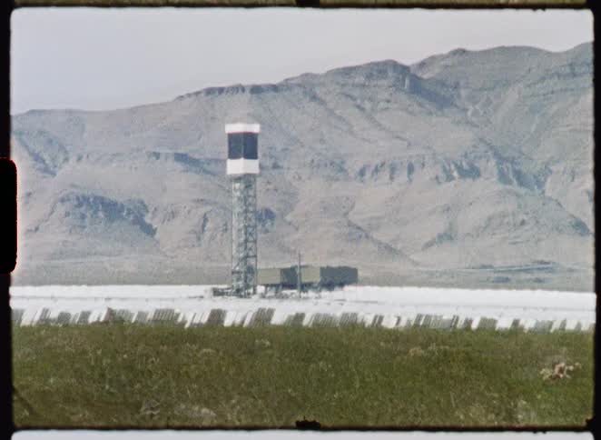 Vintage film captures a drive-by shot of a concentrated solar power plant in a vast desert landscape with mountains