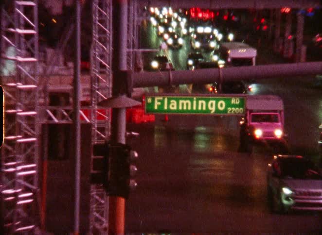 Vintage film captures the iconic Flamingo Hotel and Casino neon sign before tilting down to the bustling night traffic on Flamingo Road in Las Vegas